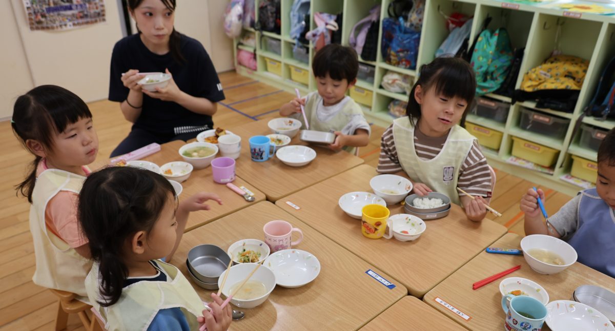 給食を食べる園児たちを見守る保育士の写真